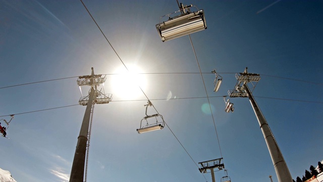 在山上的滑雪缆车下，迎着冬日的阳光和蓝天视频素材