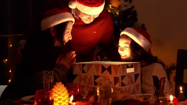 在圣诞节那天，这个幸福的家庭有了爸爸和妈妈。爸爸和妈妈送了一个奇妙的礼盒，盒子在明亮的灯光下打开。视频素材