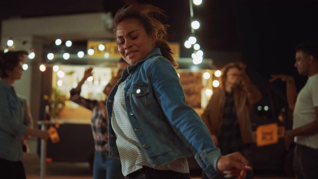 一群朋友在街头美食汉堡店外举行聚会。一个年轻美丽的女人随着音乐跳舞的肖像。这是现代街区的夜晚。每个人都是幸福的，充满喜悦视频素材