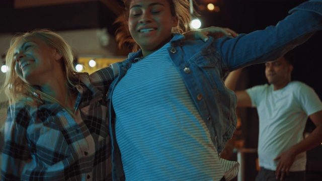 一群朋友在街头美食汉堡店外举行聚会。两个美丽的女孩随着音乐拥抱跳舞。这是现代街区的夜晚。每个人都是幸福的，充满喜悦。视频素材