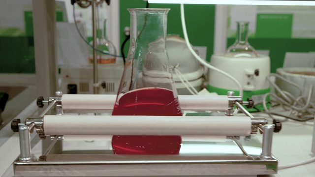 在化学实验室里，装有红色液体的玻璃烧瓶通过机械搅拌来混合。视频素材