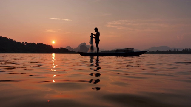 日落时分，渔民在湖边用小船准备渔网的剪影。渔民的生活方式。泰国华富里以。慢动作视频素材