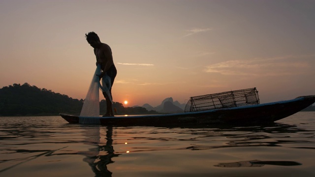 日落时分，渔民们在湖边划船，把渔网抛到一边，将渔网拉出水面。渔民的生活方式。泰国华富里以。视频素材