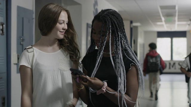 美国犹他州普罗沃，用手机跟踪拍摄在学校走廊里走路聊天的微笑女孩视频素材