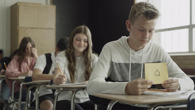 美国犹他州普罗沃，一名女孩在学校教室里向男孩传递爱的纸条视频素材