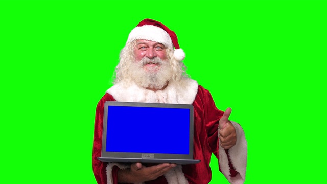 圣诞老人拿着笔记本电脑用蓝色的屏幕指着它，色度键绿色的屏幕背景视频下载