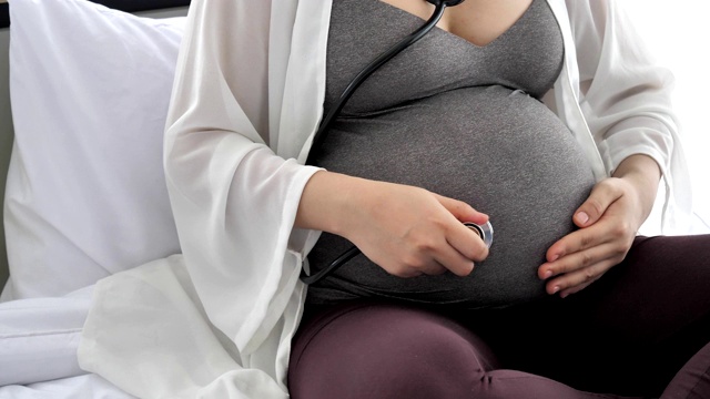 妇女孕妇在家用听诊器近距离检查腹部。健康和医学概念。新生儿和婴儿主题。视频素材