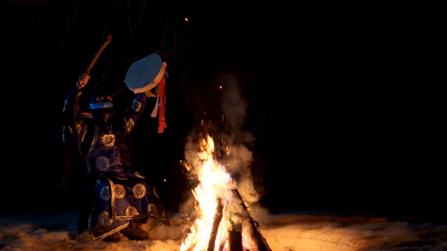 萨满坐在火边摇着，手里拿着一只小手鼓。视频下载