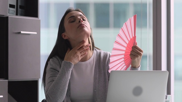 疲惫而汗流浃背的女商人挥舞着扇子在办公室里受热视频素材