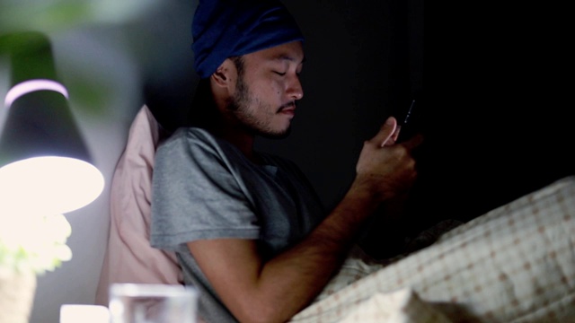 亚洲帅哥躺在床上玩手机。浏览社交媒体和看视频。视频下载