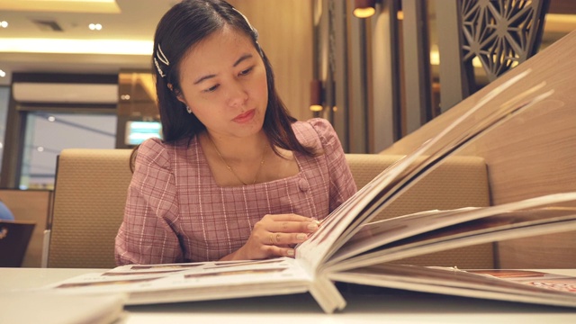 年轻亚洲女人在餐厅看菜单的慢镜头，假期周末的概念，亚洲女人的生活方式视频素材
