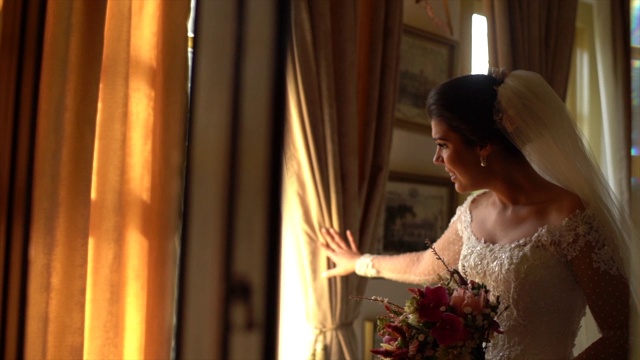 新娘手持花束，在婚礼前透过窗户看视频素材