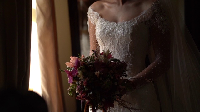 新娘手持花束，在婚礼前透过窗户看视频下载