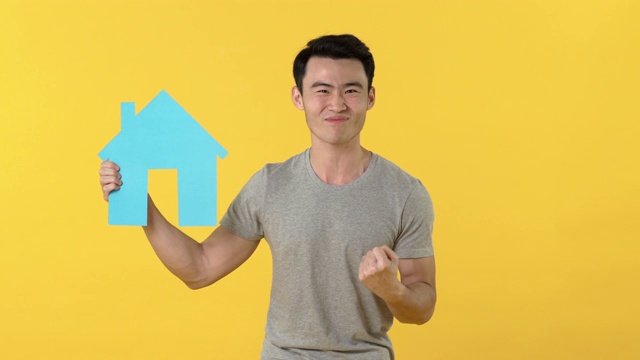年轻兴奋的亚洲人拿着黄色背景的房地产标志视频下载