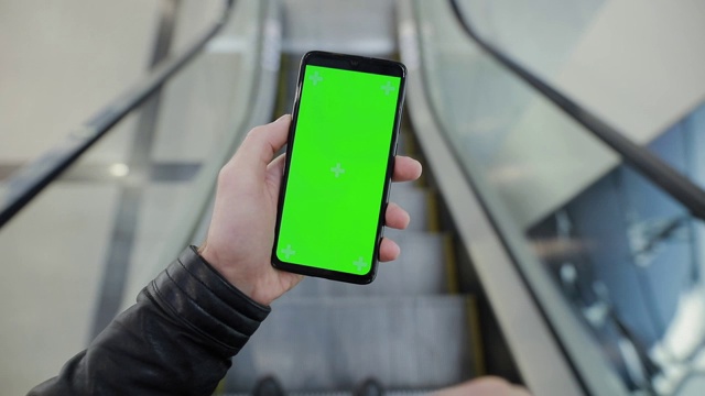 POV，男性在商场的自动扶梯上用绿色屏幕的智能手机视频素材