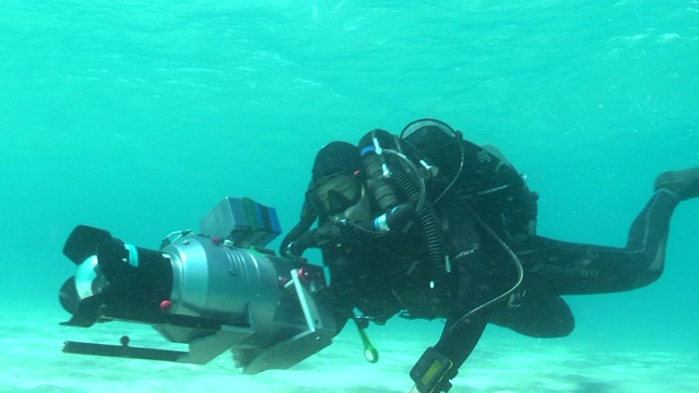 一个戴着水肺的潜水员带着一个巨大的水下摄像机游到沙底。视频下载
