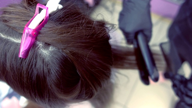 美发师在美容院用发夹将美女的深棕色头发拉直。视频素材