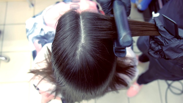 美发师在美容院用发夹将美女的深棕色头发拉直。视频素材