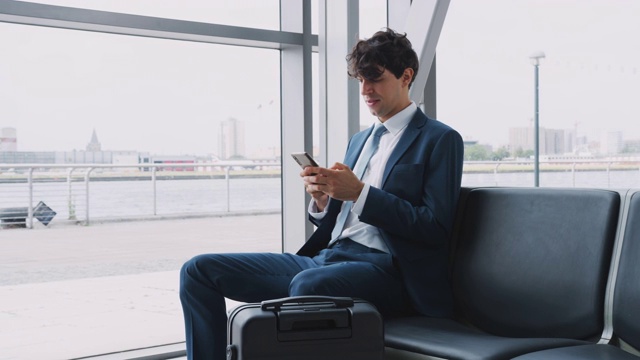 商人坐在机场候机室用手机拍摄的慢动作行李视频素材