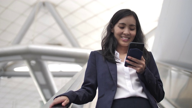 美丽的亚洲女人在自动扶梯上使用智能手机视频素材