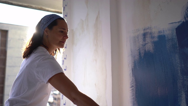 拉丁美洲专注的妇女用蓝色的油漆油漆一面墙看起来非常专注视频下载