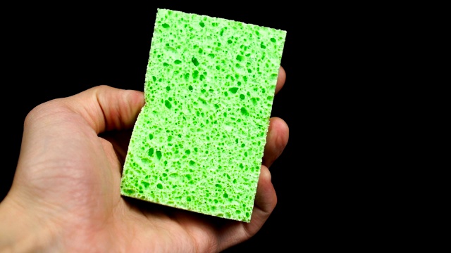 新的绿色海绵在人的手中，在黑色的背景视频下载