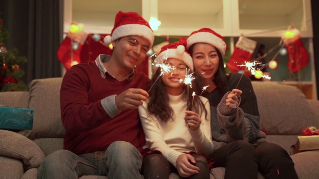 慢动作视频拍摄了一个快乐的家庭生活在一起的父亲，母亲和女儿在圣诞节玩有趣的烟花。视频素材