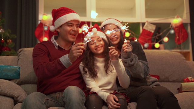 一个快乐的家庭生活在一起的慢动作视频拍摄的父亲，母亲和女儿玩有趣的烟花在圣诞节。视频素材