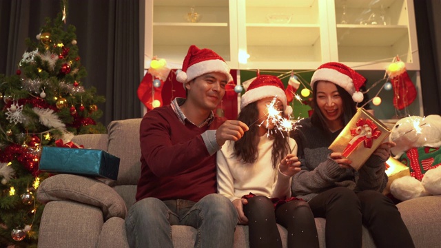 视频拍摄的一个幸福的家庭生活在一起的父亲，母亲和女儿玩有趣的烟花在圣诞节。视频素材