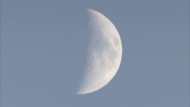 一轮白色的半月挂在白天的天空。视频下载