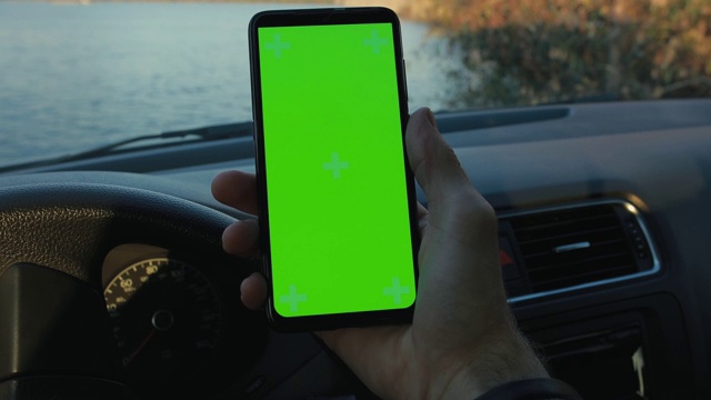 在河边的一辆车里，男性手握绿色屏幕的智能手机视频素材