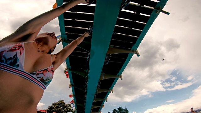 在冒险公园里，穿着比基尼的少女挂在体操环上视频素材
