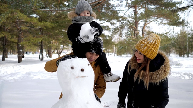 年轻的家庭，妈妈，儿子和爸爸在冬季城市公园堆雪人。视频素材