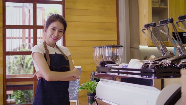 年轻微笑的亚洲女性咖啡师或女性咖啡所有者使用咖啡机，并在咖啡店咖啡厅看着镜头视频素材