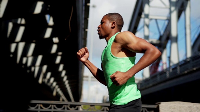 腰部以上跟踪左慢动作镜头的年轻非洲运动员呼吸正确，而跑下城市大桥视频下载