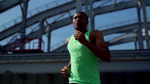 腰部以上的慢动作镜头确定男非洲运动员在城市桥梁下跑在绿色坦克背心马拉松训练视频下载