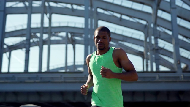 腰部以上的镜头，肌肉发达的非洲运动员在绿色背心跑在步行桥和城市桥下路在夏天的一天视频下载