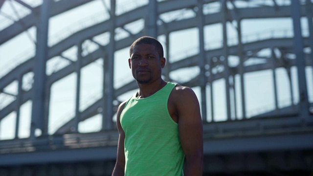 镜头转向腰部以上的非洲运动员站在城市大桥上，自信地看着镜头视频下载