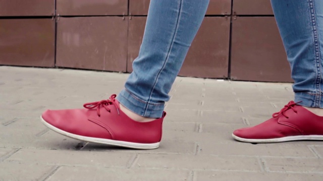 一个女人在秋天的白天走在城市里，近距离看她的红鞋，散步视频素材