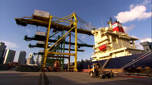 一辆卡车拖着一辆平板拖车经过一艘停靠在新加坡港口集装箱码头的船。视频素材