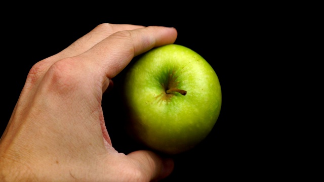 男性的手拿着一个绿苹果在一个黑色的背景视频素材