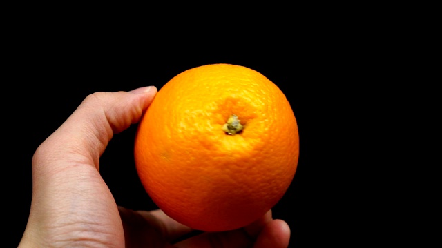 男性的手拿着一个橙色的柑橘在一个黑色的背景视频素材