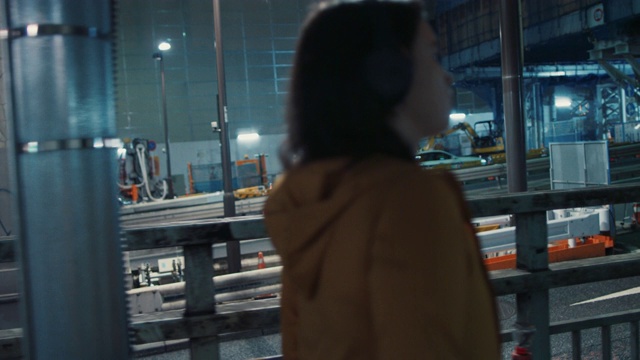 在日本东京，一名年轻女子戴着耳机走在夜里视频下载
