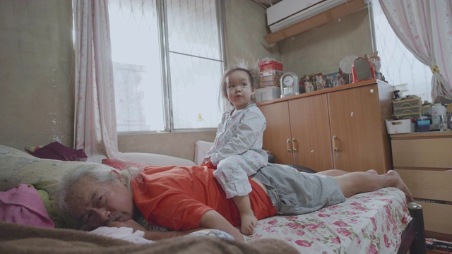 慢动作亚洲小女孩与爷爷在床上玩耍。视频素材