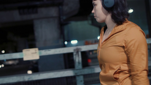 在日本东京，一名年轻女子调整着耳机，走在夜里视频下载