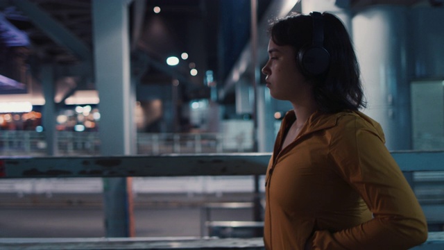 在日本东京，一名年轻女子戴着耳机走在夜里视频素材