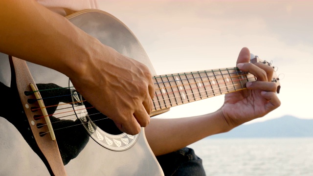 4 k。一个男人在海滩上弹奏吉他的特写，在日落时分，感觉很放松视频下载