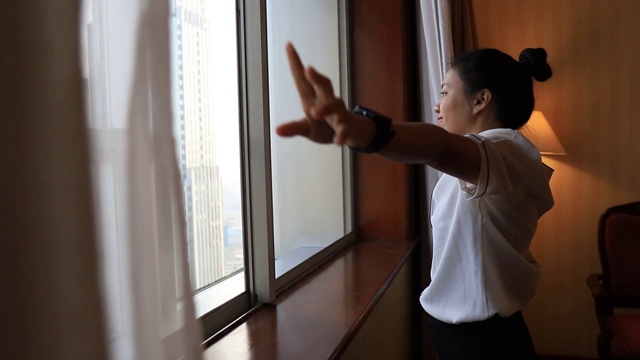 亚洲女性住在酒店房间里。打开房间里的窗帘，看外面的景色。假日旅游概念。视频素材