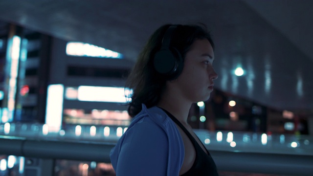 一名年轻女子戴着运动胸罩和耳机在日本东京的夜晚散步视频下载