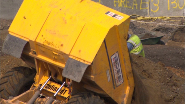 挖掘机把土倒进建筑工人旁边的一个堆里。视频素材